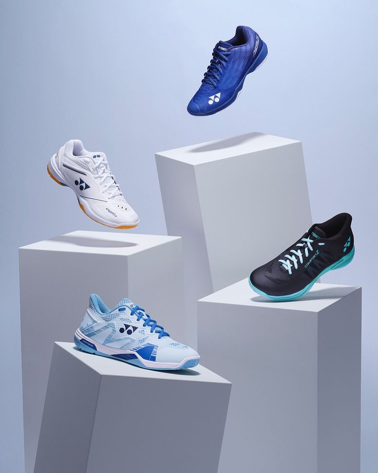 Professional product photography of four Yonex badminton shoes displayed on minimalist white podiums with a clean studio background