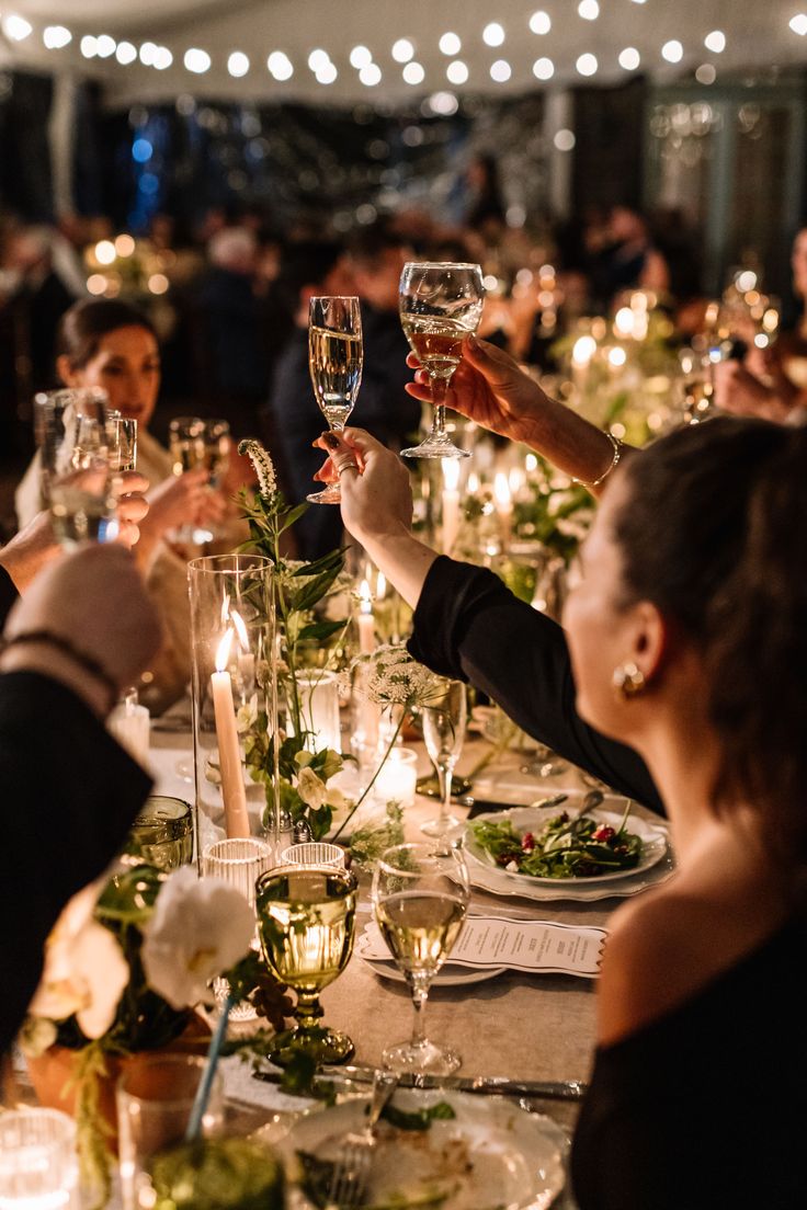 Guests raising wine glasses in a toast during an elegant candlelit dinner event, captured with warm ambient lighting and professional event photography